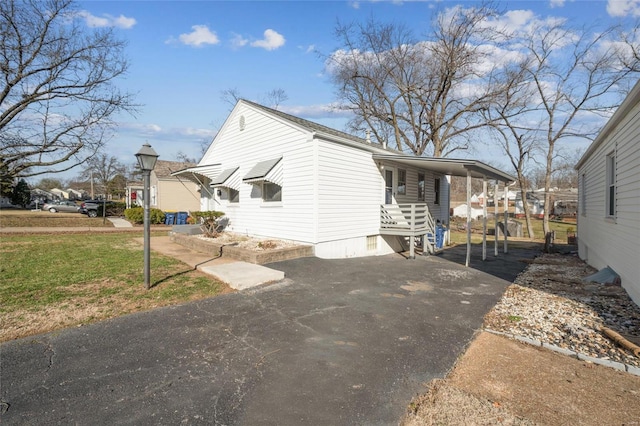 view of property exterior with aphalt driveway, a lawn, and a carport