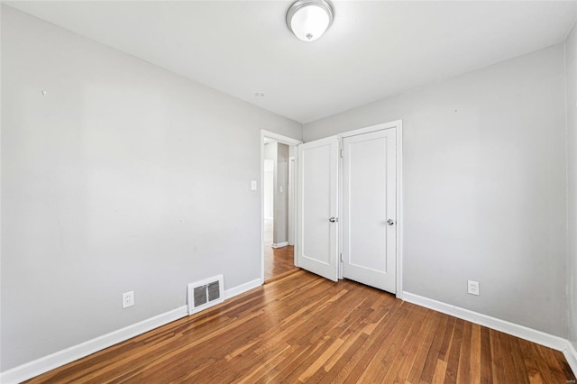 unfurnished bedroom featuring hardwood / wood-style flooring, baseboards, visible vents, and a closet