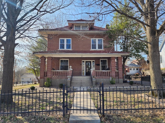 american foursquare style home featuring brick siding, a porch, a fenced front yard, and a gate