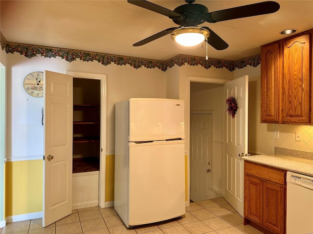 kitchen featuring tasteful backsplash, light countertops, light tile patterned floors, brown cabinets, and white appliances