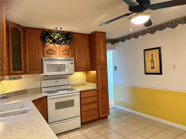 kitchen featuring glass insert cabinets, light countertops, light tile patterned flooring, white appliances, and a sink