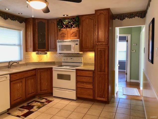 kitchen featuring brown cabinetry, white appliances, light tile patterned flooring, and a sink