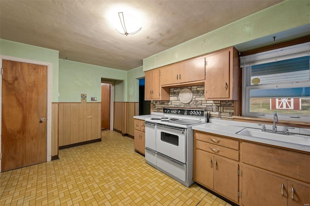 kitchen featuring wooden walls, a wainscoted wall, a sink, light countertops, and white electric range