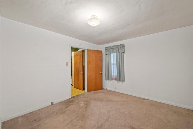 carpeted empty room featuring a textured ceiling and baseboards