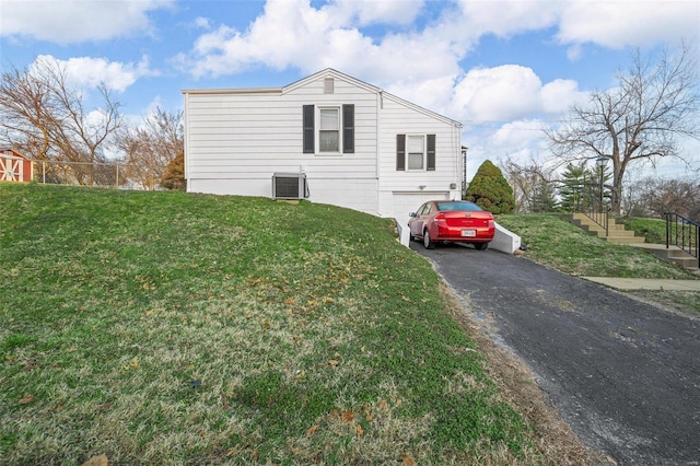 view of side of home with cooling unit, a lawn, driveway, and an attached garage