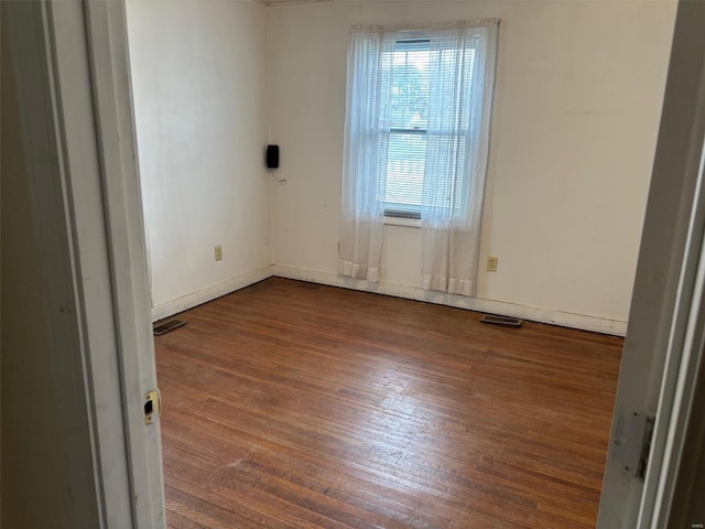 spare room with wood-type flooring, visible vents, and baseboards