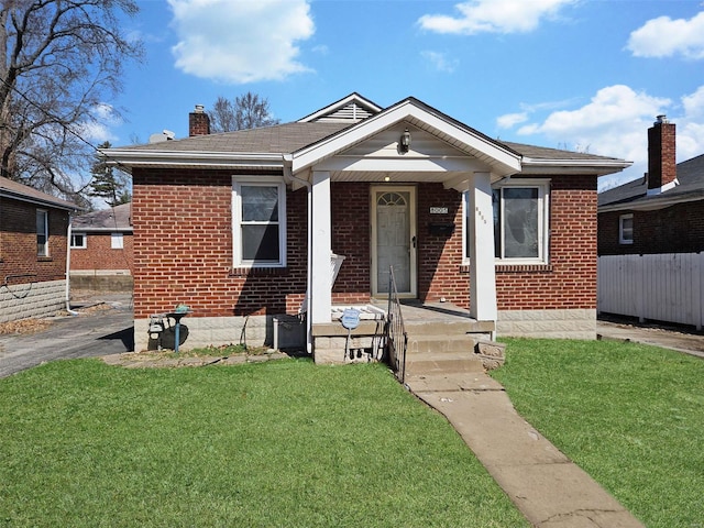 bungalow with brick siding, a front lawn, a chimney, and fence