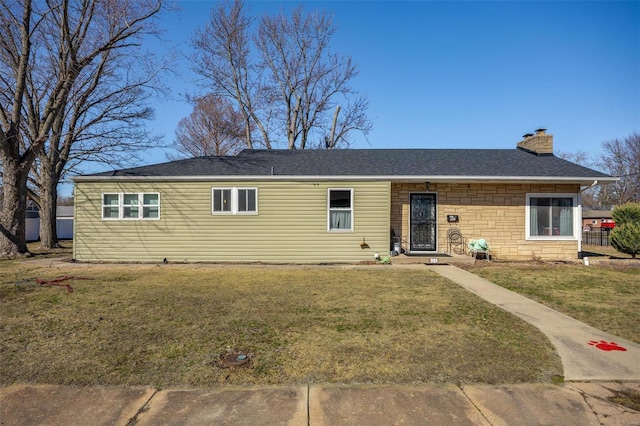 ranch-style home featuring a shingled roof, a front yard, stone siding, and a chimney