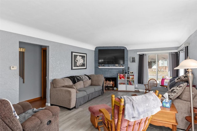 living room featuring a large fireplace, a textured wall, light wood-style flooring, and baseboards