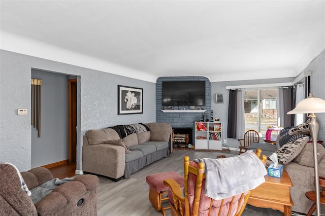 living room with a textured wall, light wood-type flooring, a fireplace, and baseboards