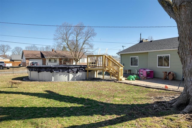 rear view of property featuring fence, roof with shingles, a lawn, a wooden deck, and a covered pool