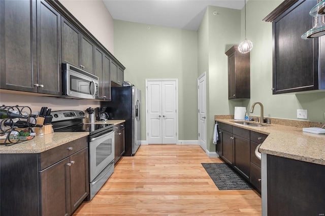 kitchen featuring baseboards, light wood-type flooring, appliances with stainless steel finishes, a towering ceiling, and a sink