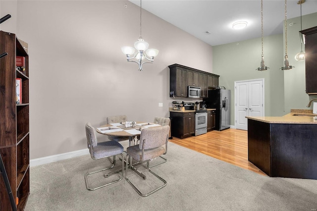 dining area with baseboards, high vaulted ceiling, light wood-style floors, a notable chandelier, and light colored carpet