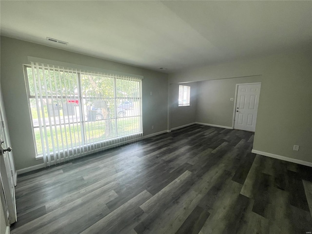 empty room featuring visible vents, dark wood finished floors, and baseboards