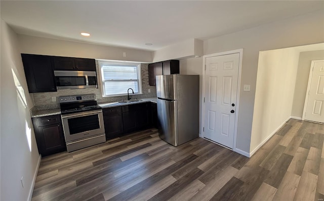 kitchen with baseboards, dark wood-type flooring, a sink, stainless steel appliances, and backsplash