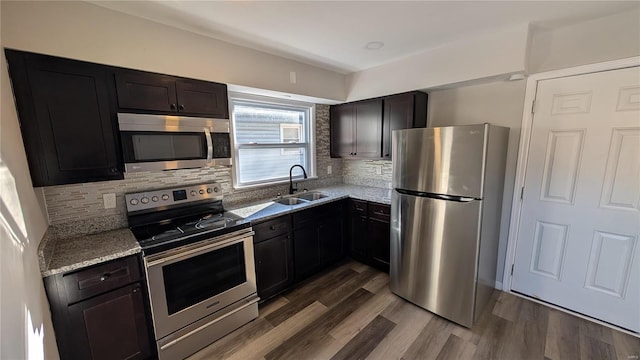 kitchen featuring appliances with stainless steel finishes, a sink, backsplash, and wood finished floors