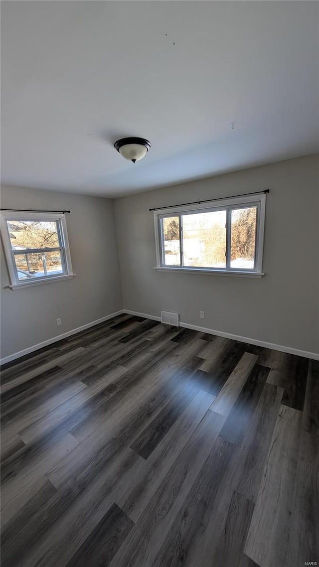 empty room with dark wood-style floors, visible vents, and baseboards