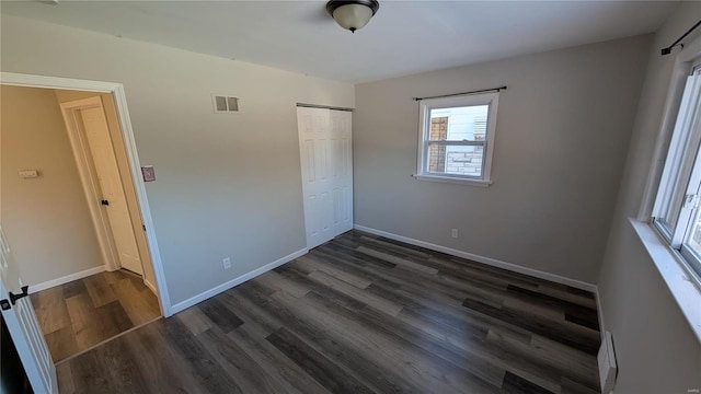 unfurnished bedroom with a closet, dark wood finished floors, visible vents, and baseboards