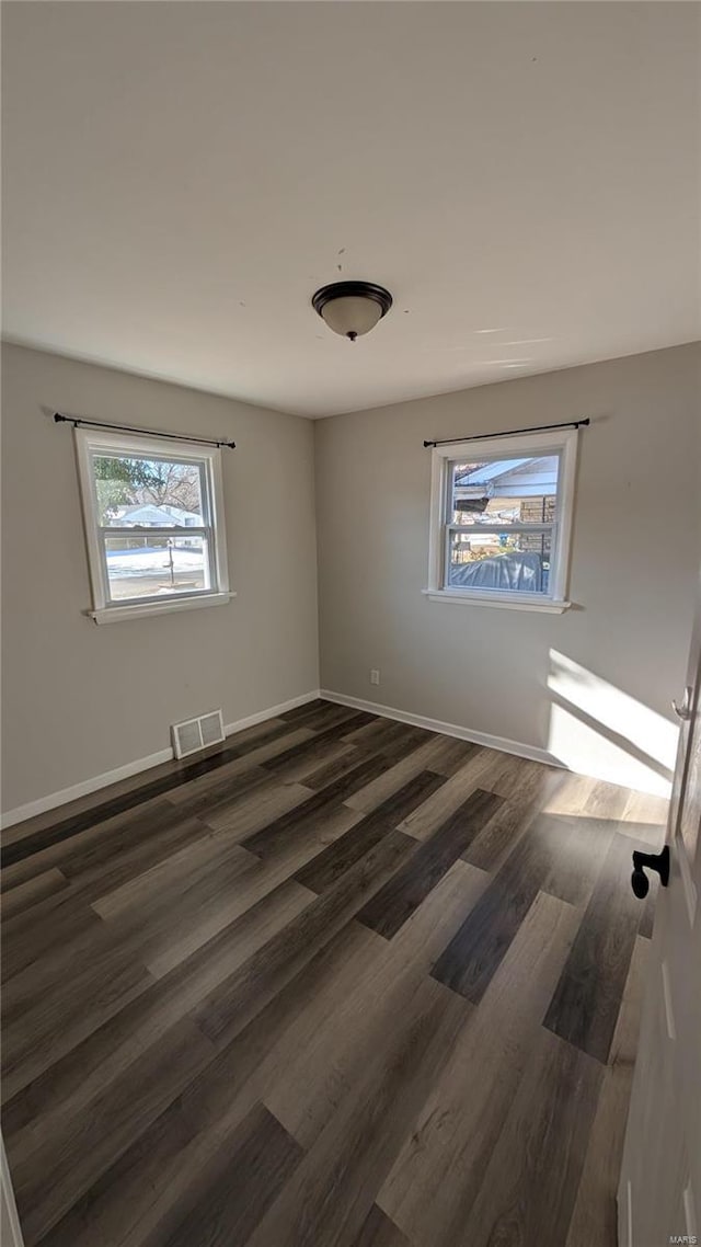 spare room featuring dark wood-style flooring, visible vents, and baseboards