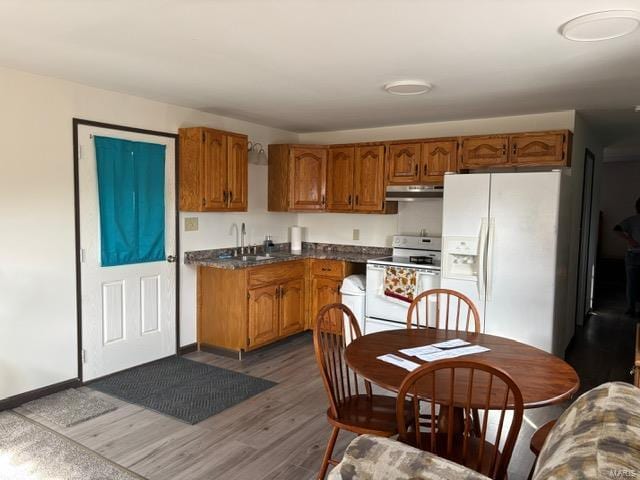 kitchen featuring dark wood finished floors, brown cabinetry, a sink, white appliances, and under cabinet range hood