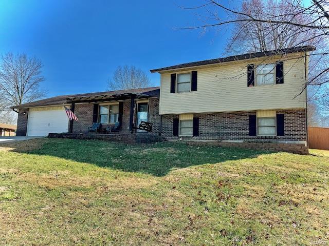 tri-level home with brick siding, an attached garage, and a front yard