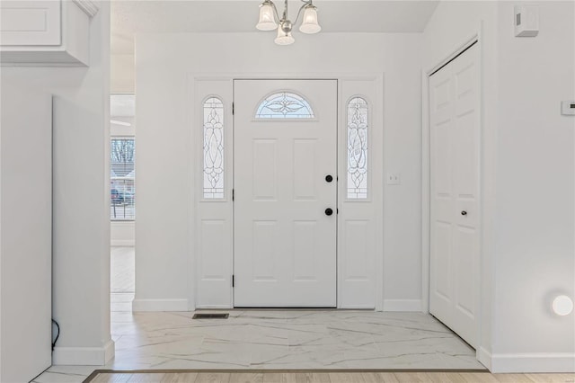 entryway with a chandelier, marble finish floor, and baseboards