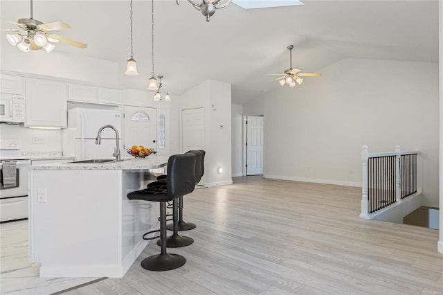 kitchen with white appliances, a skylight, light wood finished floors, a breakfast bar, and a sink