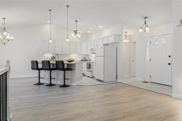 kitchen with white appliances, light countertops, light wood-style floors, a kitchen bar, and white cabinetry