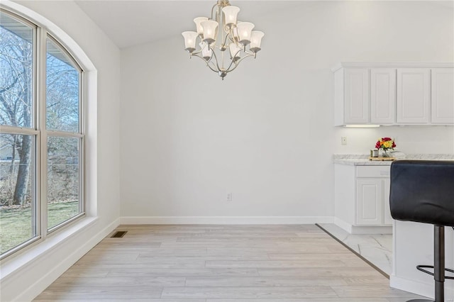 unfurnished dining area with visible vents, light wood finished floors, baseboards, and an inviting chandelier