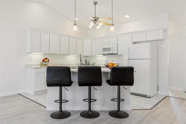 kitchen featuring light countertops, white appliances, a breakfast bar, and white cabinets