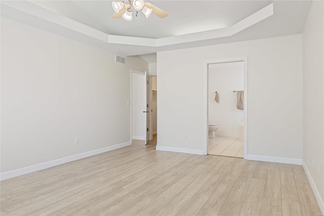 unfurnished bedroom featuring connected bathroom, visible vents, baseboards, light wood finished floors, and a raised ceiling