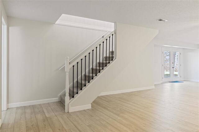 stairway featuring a textured ceiling, wood finished floors, visible vents, baseboards, and french doors