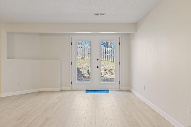 doorway featuring a textured ceiling, visible vents, baseboards, french doors, and light wood finished floors