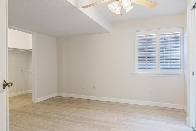 unfurnished bedroom with baseboards, light wood-style flooring, a spacious closet, a textured ceiling, and a closet