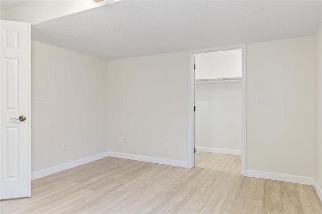 unfurnished bedroom featuring light wood finished floors, a spacious closet, baseboards, and a textured ceiling