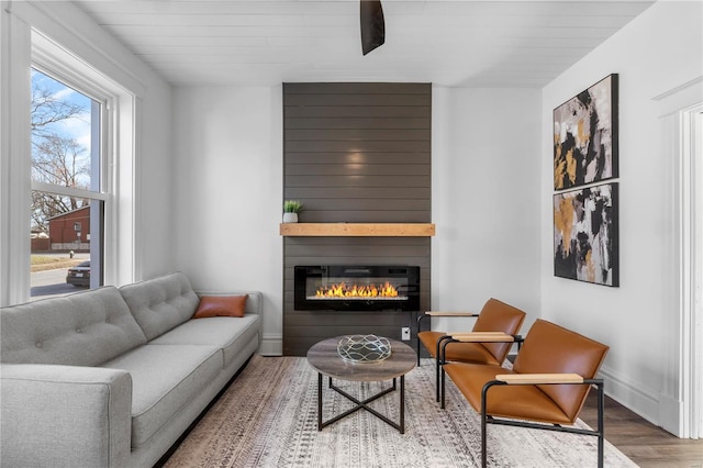 living room featuring wood finished floors, baseboards, and a large fireplace