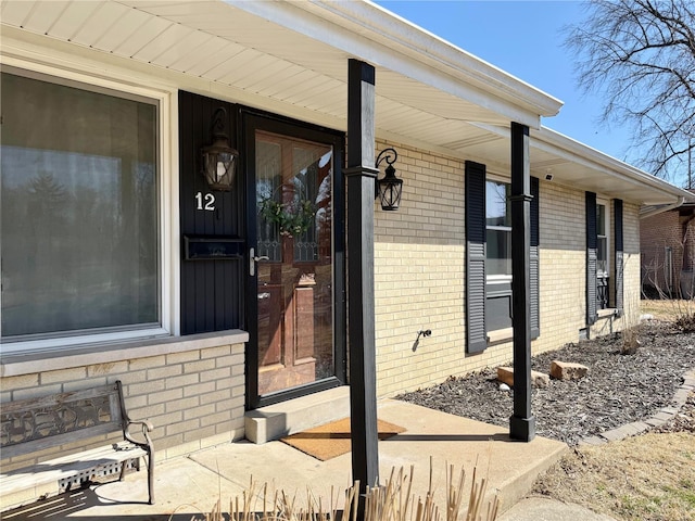 view of exterior entry featuring brick siding and a porch