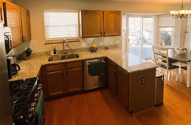 kitchen with appliances with stainless steel finishes, dark wood-type flooring, a peninsula, and a sink