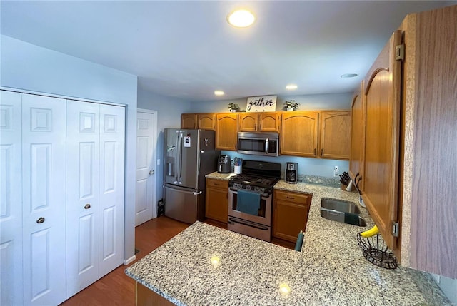 kitchen featuring brown cabinets, a sink, light stone counters, stainless steel appliances, and a peninsula