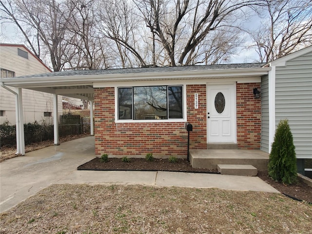 doorway to property with a carport, brick siding, and driveway