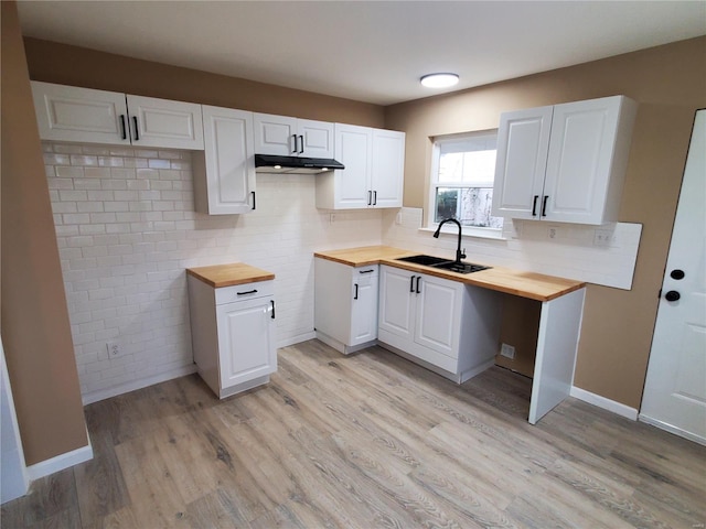 kitchen with light wood finished floors, white cabinetry, wooden counters, and a sink