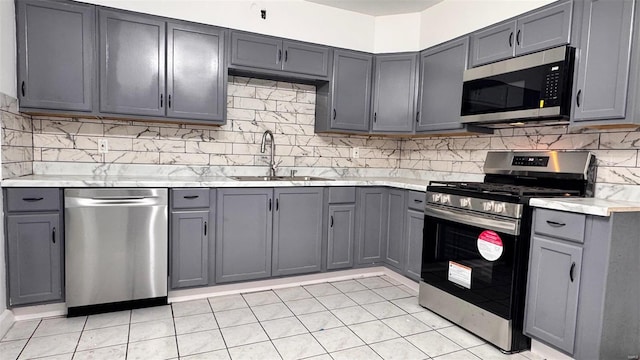 kitchen with a sink, gray cabinets, backsplash, and stainless steel appliances