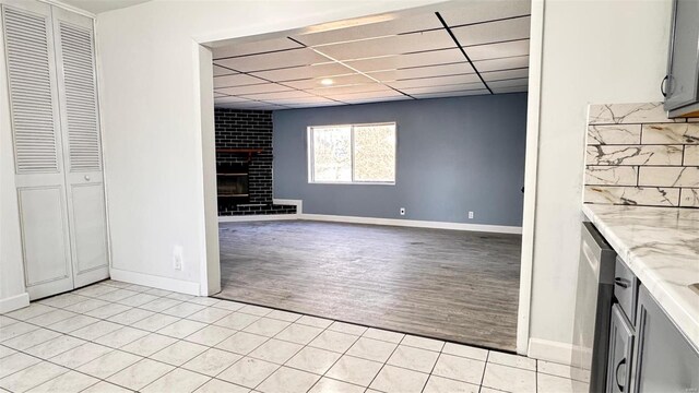 interior space featuring light wood-style flooring, a fireplace, baseboards, and a drop ceiling