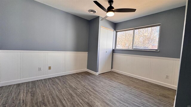 unfurnished room featuring ceiling fan, visible vents, a wainscoted wall, and wood finished floors