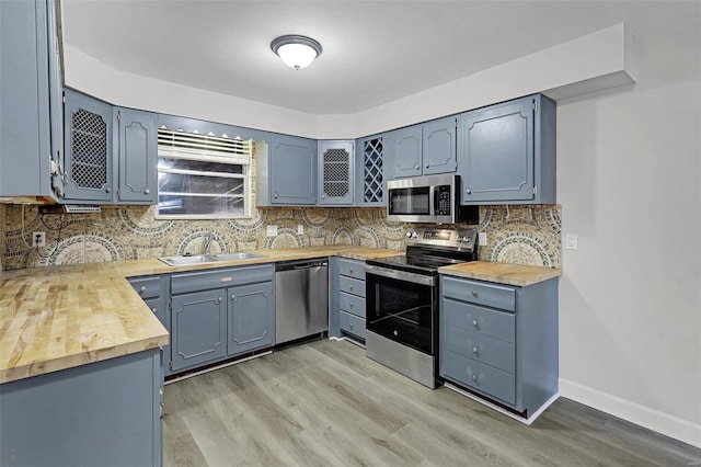 kitchen with tasteful backsplash, butcher block countertops, appliances with stainless steel finishes, light wood-style floors, and a sink