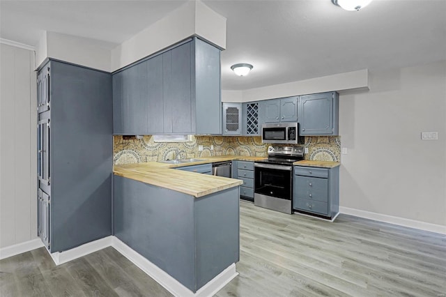 kitchen with light wood-style flooring, gray cabinetry, a peninsula, appliances with stainless steel finishes, and tasteful backsplash