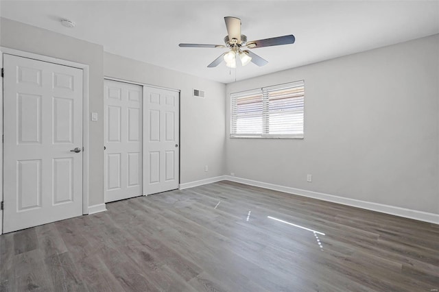 unfurnished bedroom with ceiling fan, wood finished floors, visible vents, baseboards, and a closet