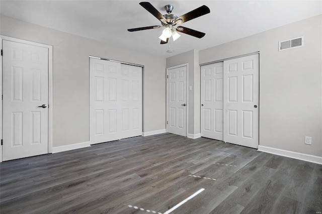 unfurnished bedroom featuring multiple closets, baseboards, visible vents, and dark wood-type flooring