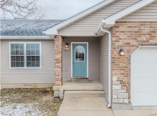 doorway to property with a garage, brick siding, and a shingled roof