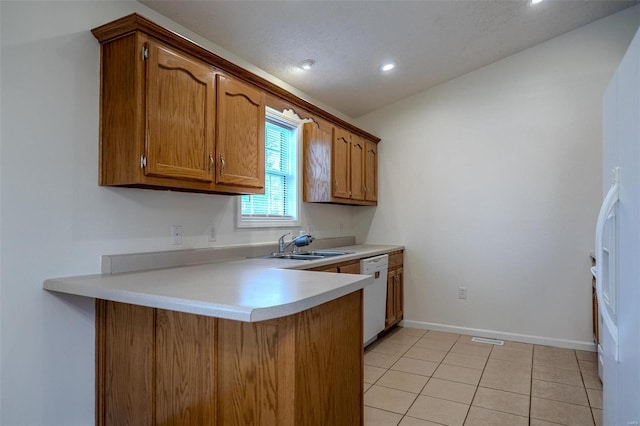 kitchen with brown cabinets, light countertops, light tile patterned flooring, white appliances, and a peninsula